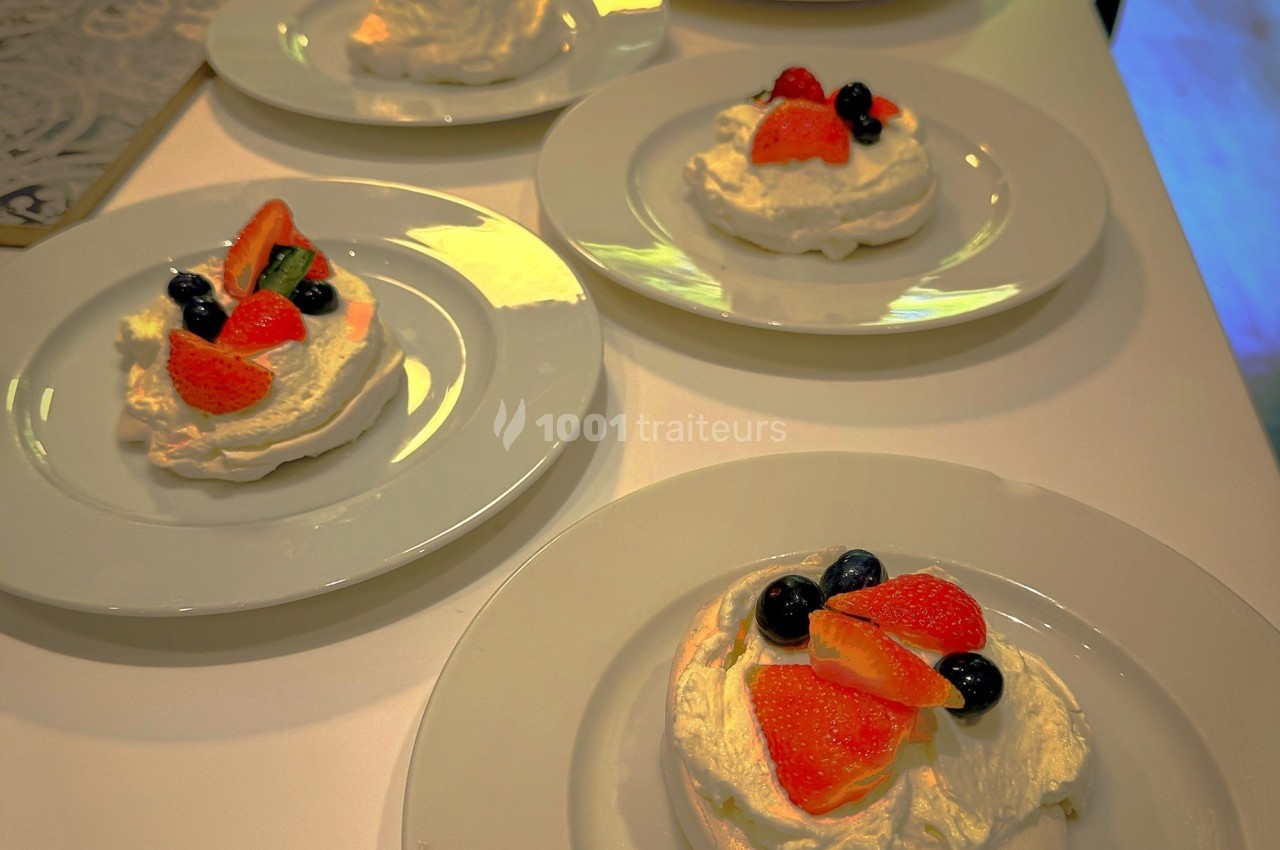 Assiettes de pavlovas individuelles garnies de fraises, myrtilles et crème fouettée, disposées sur une table blanche.