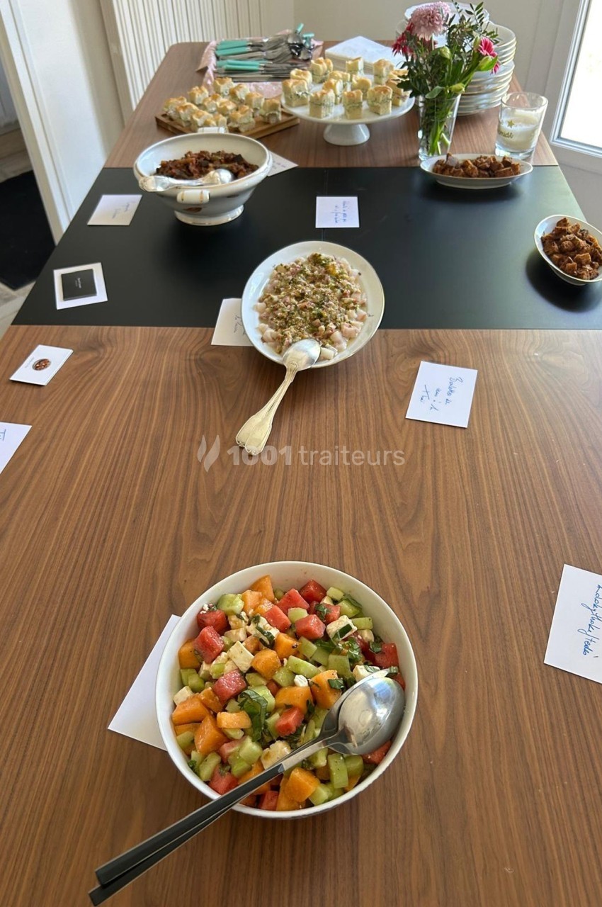 Table en bois avec plusieurs plats variés, dont une salade de fruits au premier plan, disposés pour un buffet.