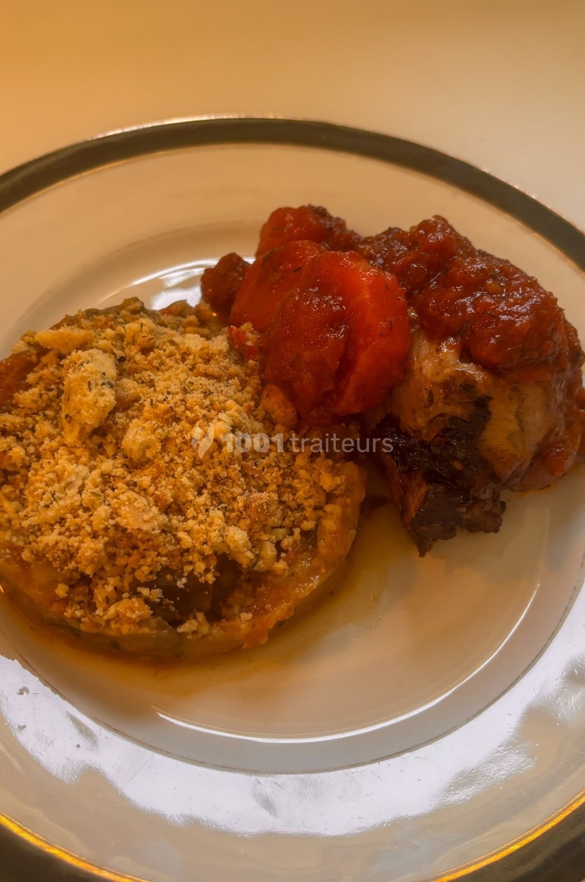 Assiette contenant un crumble de légumes et une portion de viande en sauce tomate, servie sur une table.