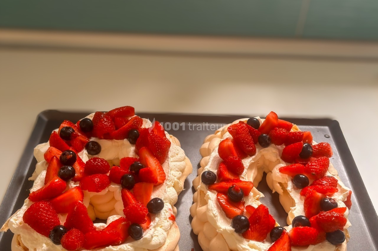 Pavlovas en forme de chiffres 8 et 0, garnies de crème, fraises, framboises et myrtilles sur un plateau noir.