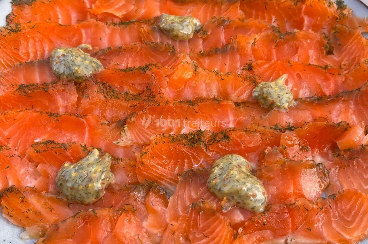 Tranches de saumon gravlax garnies de petites touches de sauce moutarde à l'aneth, présentées sur une assiette.