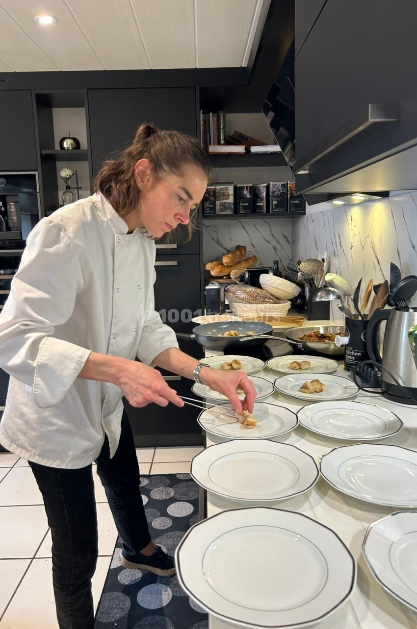 Une cheffe en cuisine dispose des amuse-bouches sur des assiettes blanches alignées sur un plan de travail.