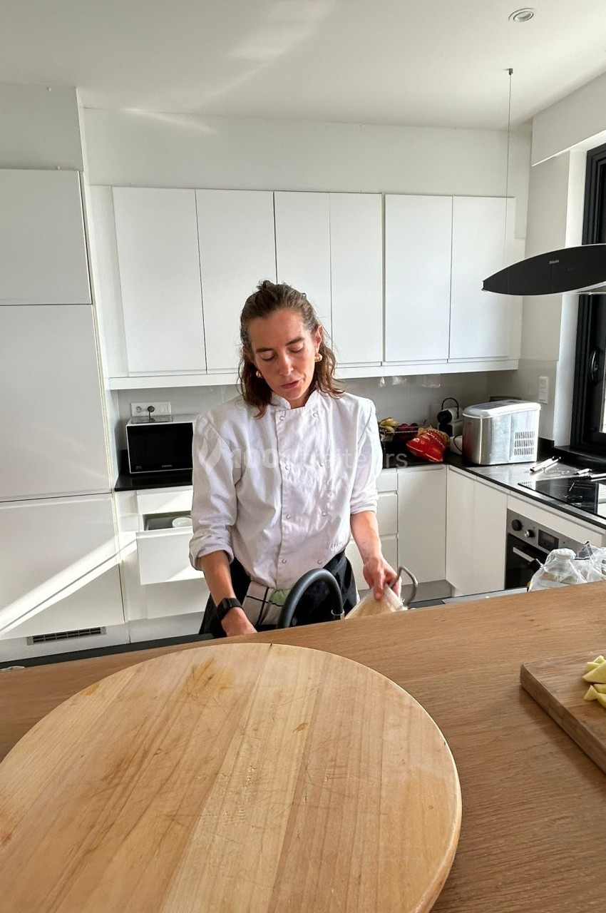 Une femme en tenue de cuisine nettoie un ustensile dans une cuisine moderne et lumineuse.