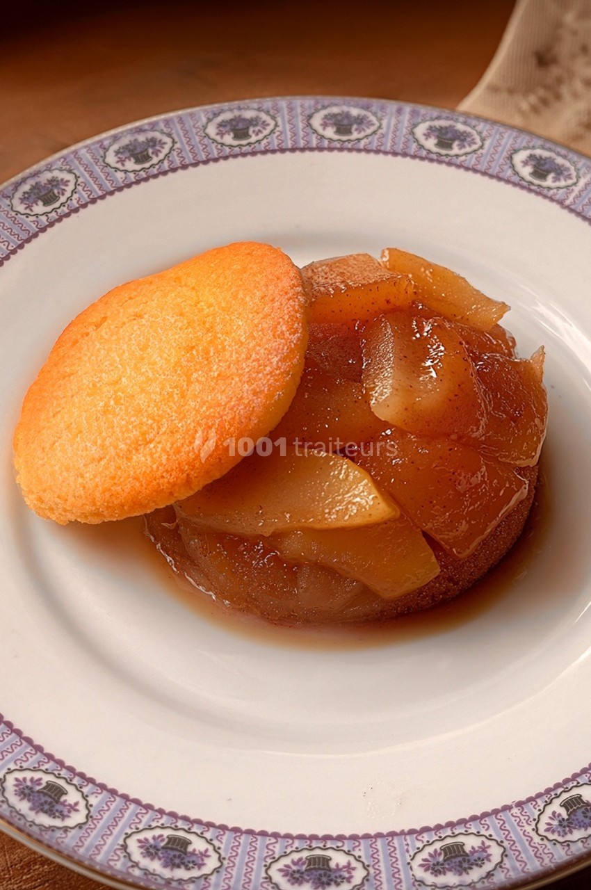 Dessert composé de pommes caramélisées surmontées d'un biscuit doré, présenté dans une assiette décorative.