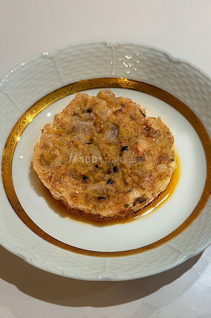 Tartare de poisson présenté dans une assiette blanche bordée de doré, avec une sauce légèrement brillante.
