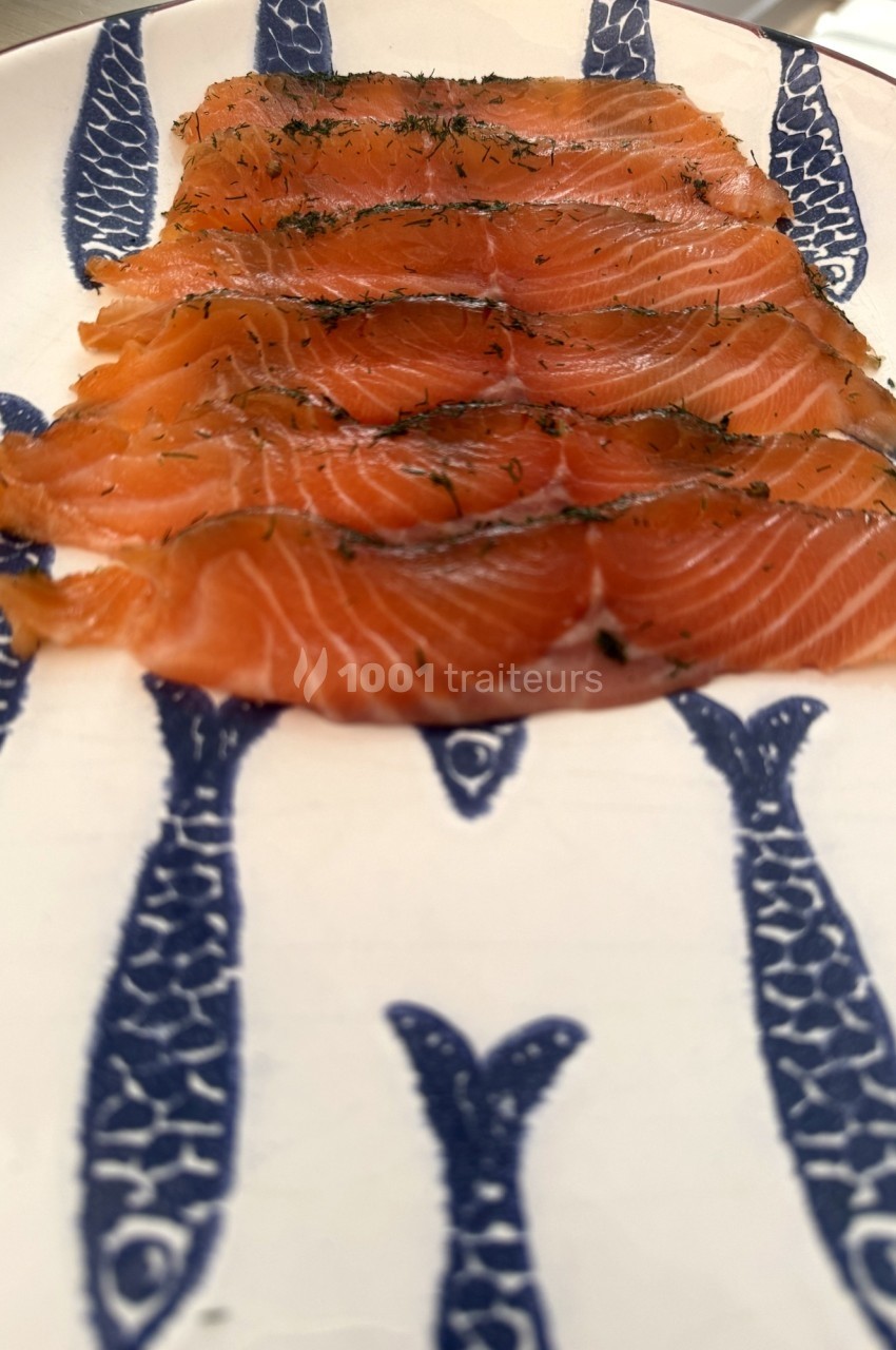 Tranches de saumon fumé disposées sur une assiette décorée de motifs de poissons bleus.