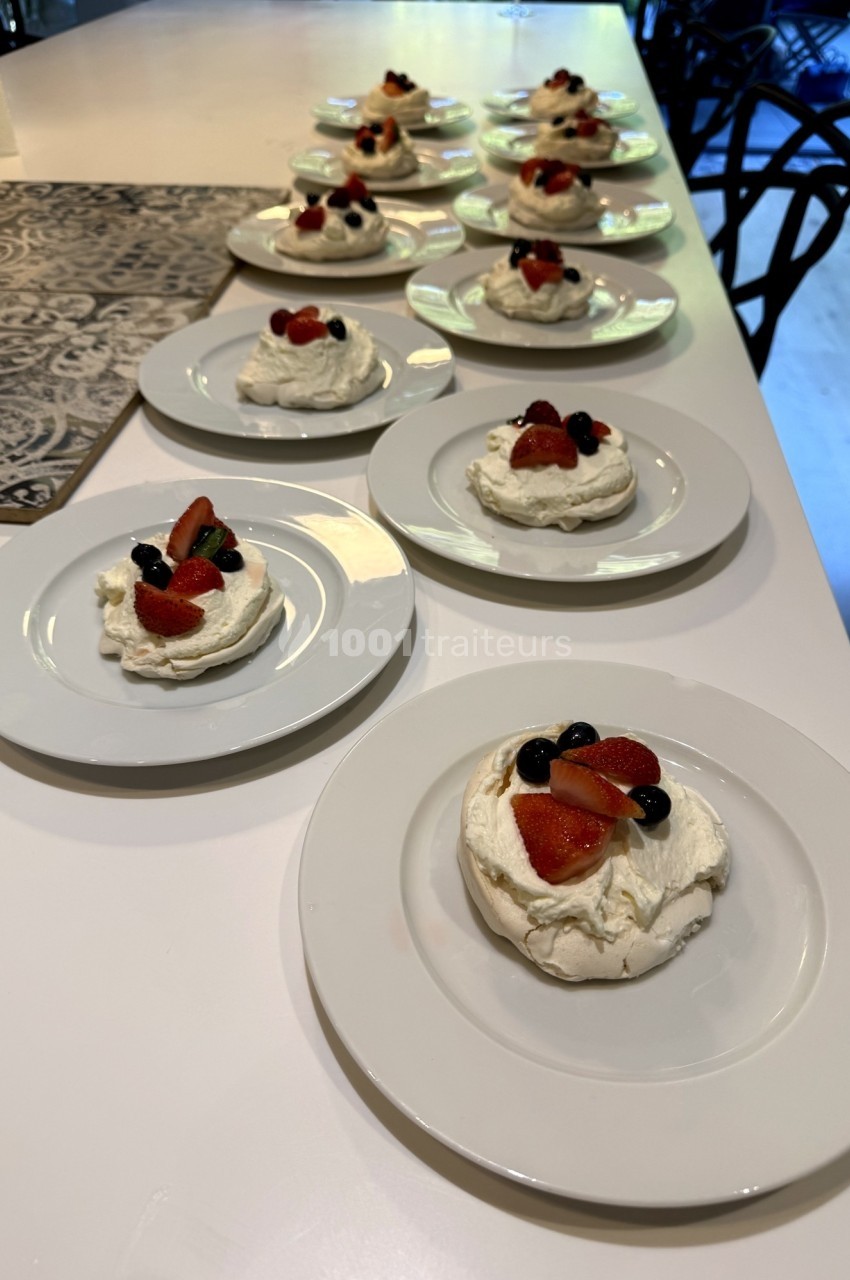 Assiettes de pavlovas individuelles garnies de fraises, myrtilles et kiwis, disposées sur une table blanche.