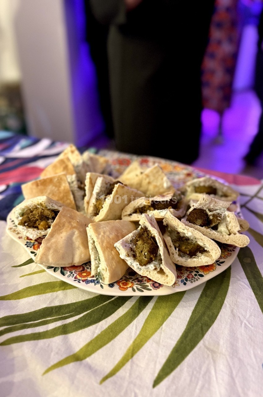 Assiette de mini sandwichs pita garnis de falafels et de sauce, présentée sur une nappe colorée.