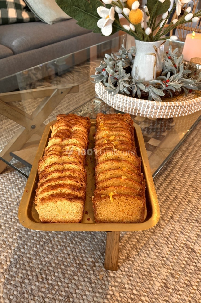 Tranches de gâteau doré disposées sur un plateau doré, posé sur une table basse en verre dans un salon décoré.