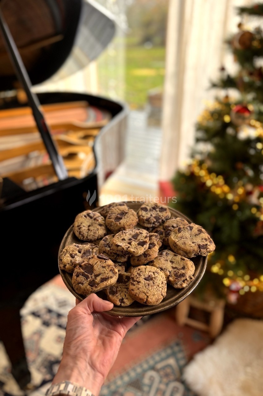 Assiette de cookies aux pépites de chocolat tenue devant un piano à queue et un sapin décoré.