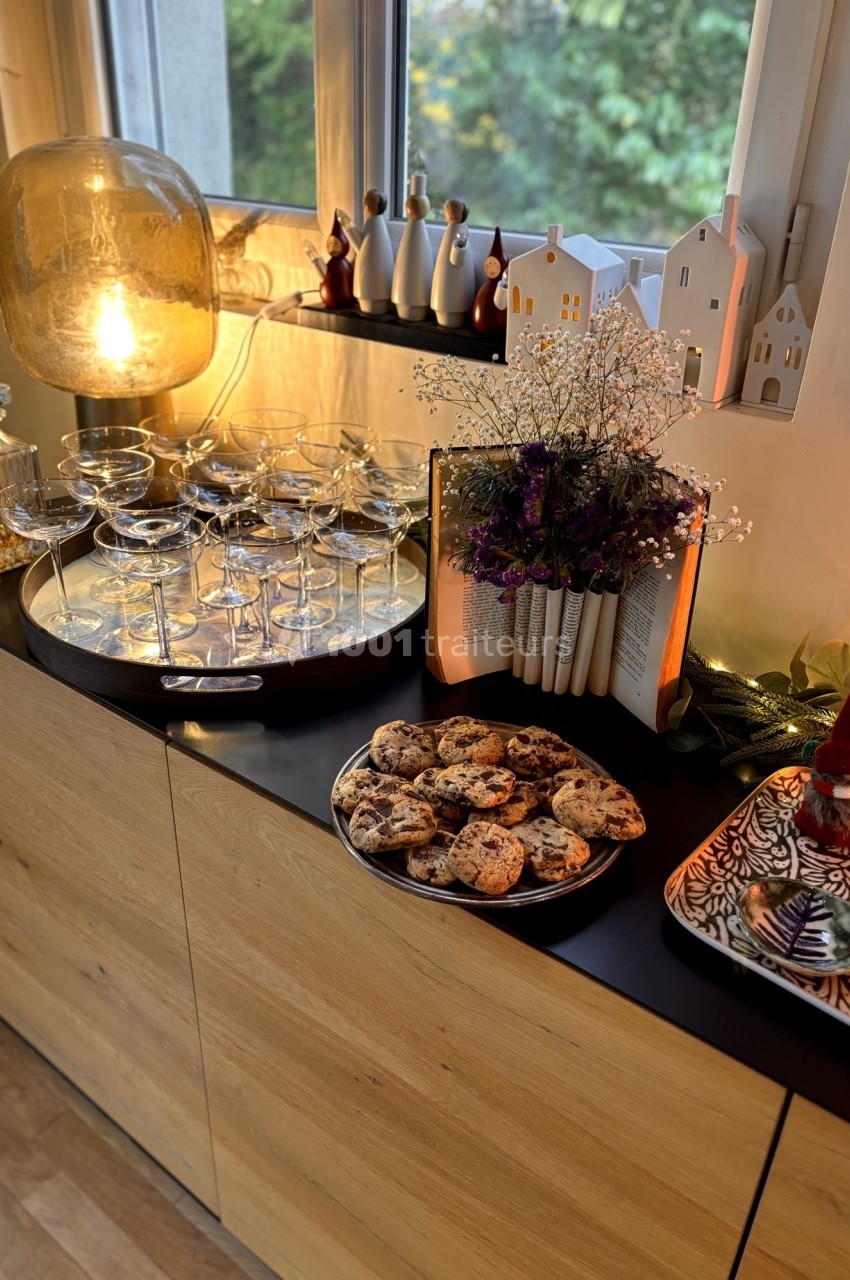 Plateau de coupes en verre, biscuits aux pépites de chocolat et décorations lumineuses sur un buffet en bois.