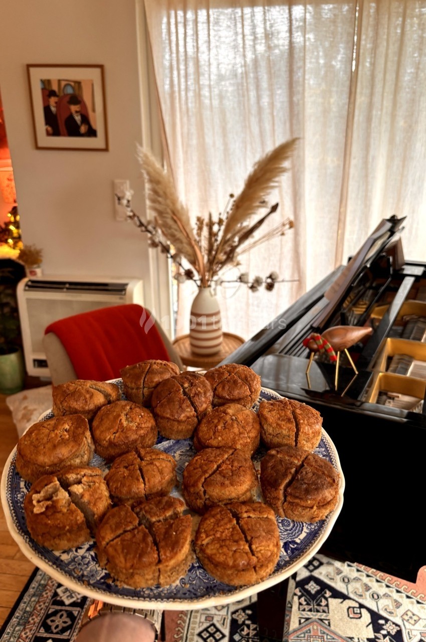 Assiette de petits pains dorés posée devant un salon chaleureux avec un piano, des plantes et une décoration cosy.