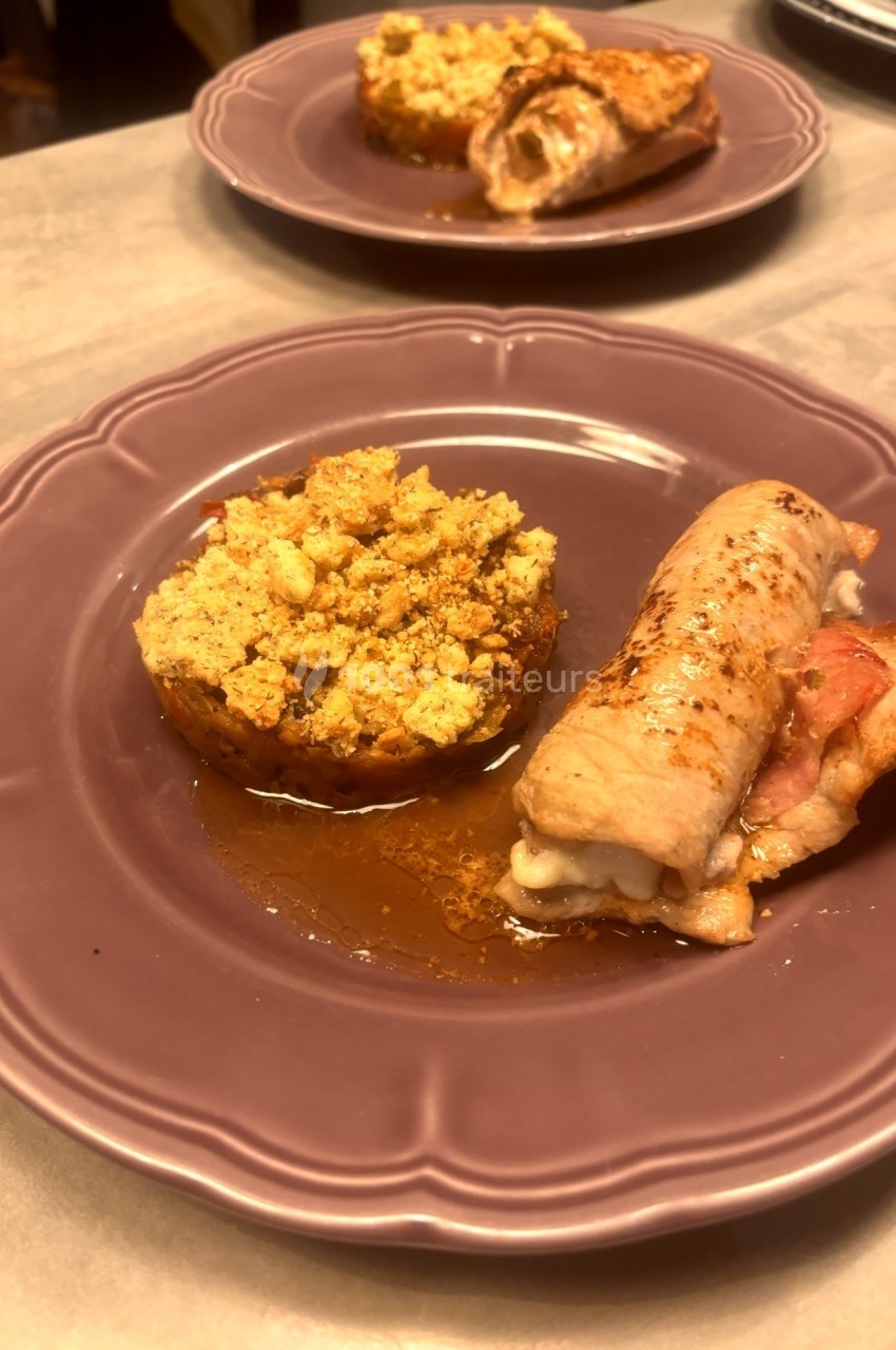 Assiette contenant un roulé de viande farci et une tomate garnie de chapelure dorée, présentée sur une table.