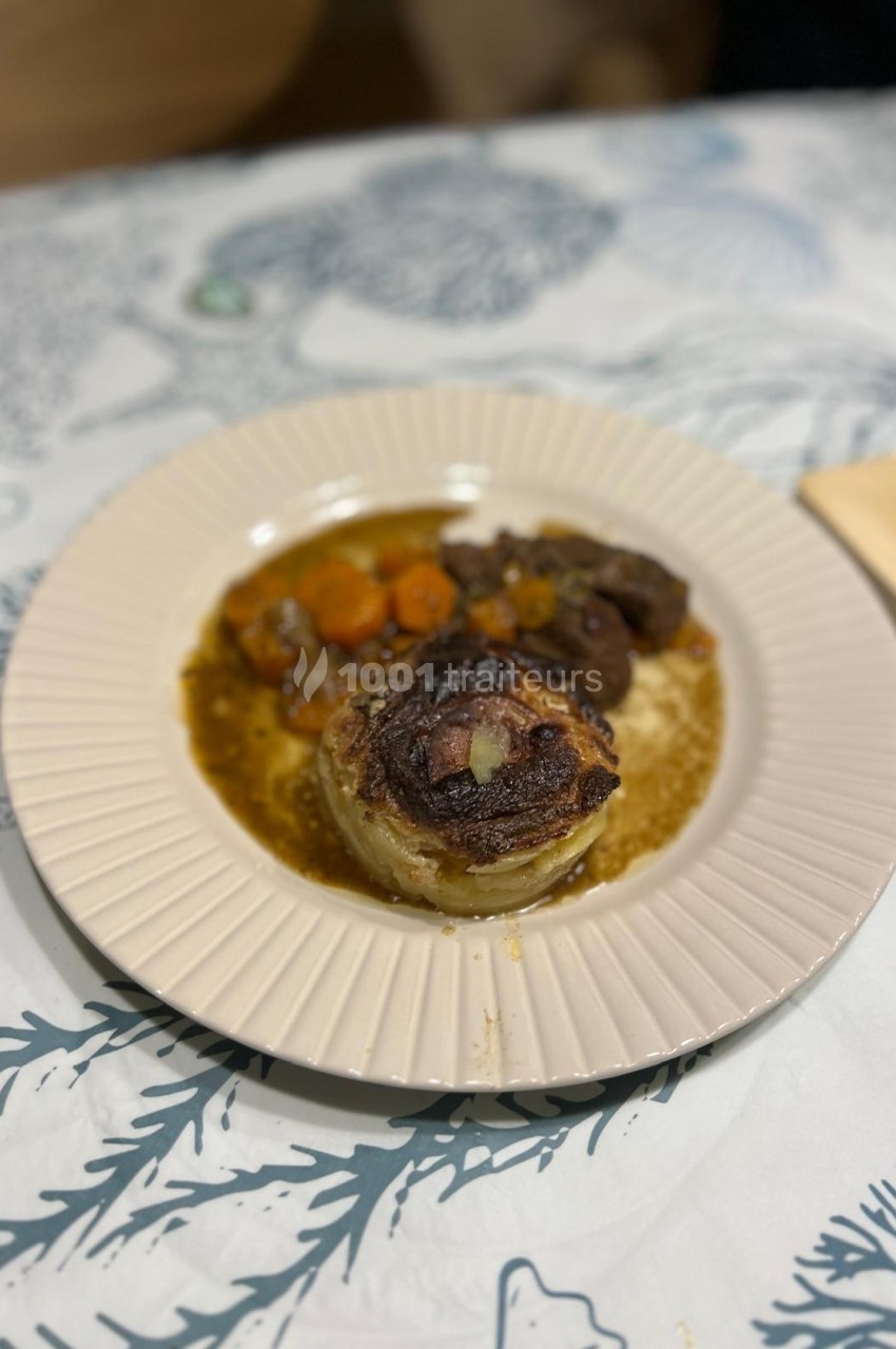 Assiette contenant un plat de viande en sauce avec des légumes, servie sur une nappe à motifs marins.