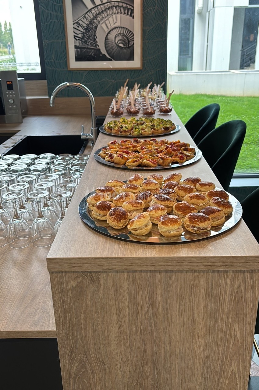 Plateau de bouchées salées variées disposé sur un comptoir en bois, avec des verres alignés à gauche.