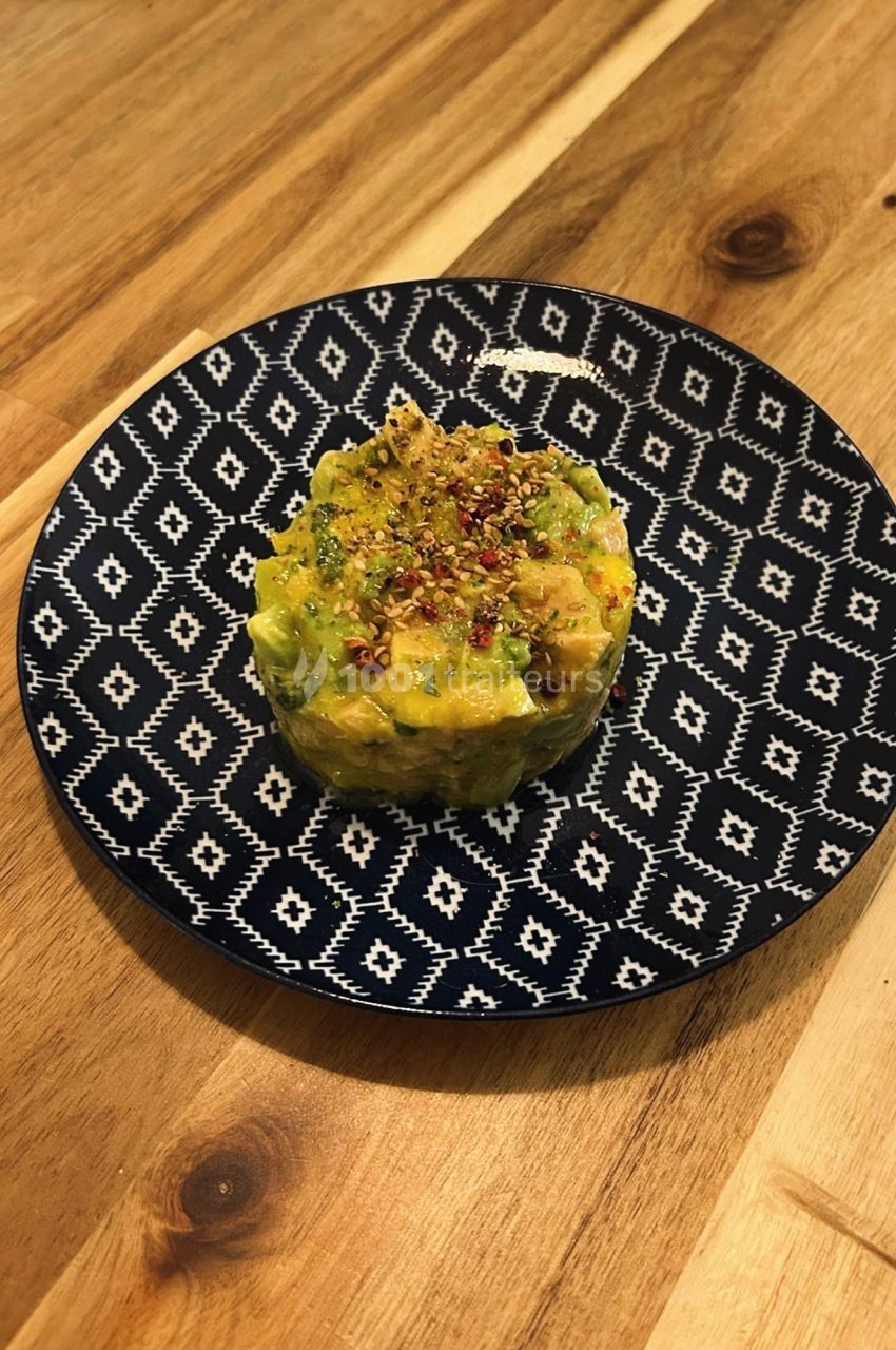 Tartare d'avocat et mangue, garni d'épices, présenté sur une assiette à motifs géométriques.