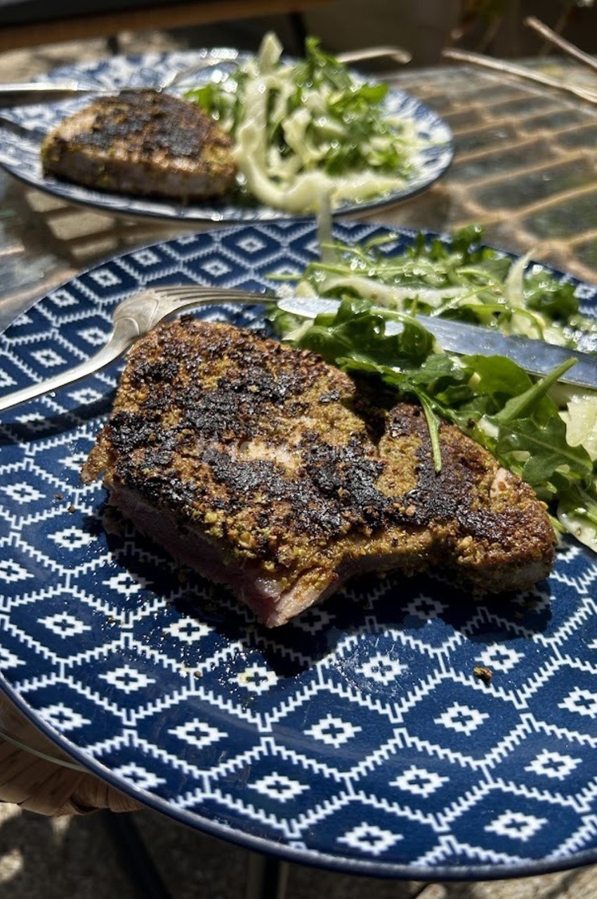 Assiette contenant un steak grillé avec une salade verte et de fenouil, posée sur une table en extérieur.