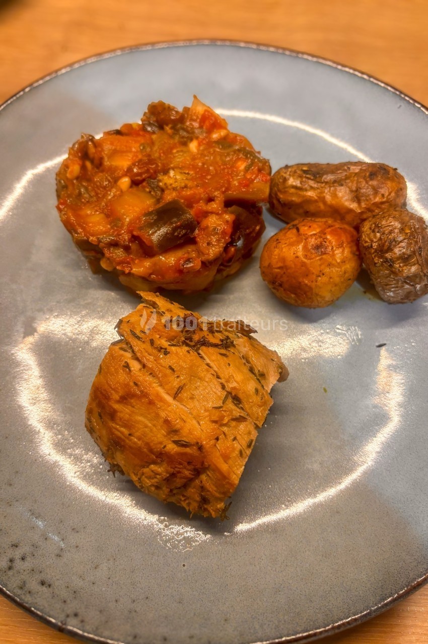 Assiette contenant un morceau de viande, une portion de ratatouille et des pommes de terre rôties.