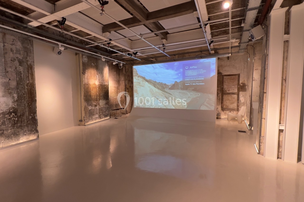 Salle minimaliste avec murs en béton brut, sol clair et projection d'une image sur un mur.