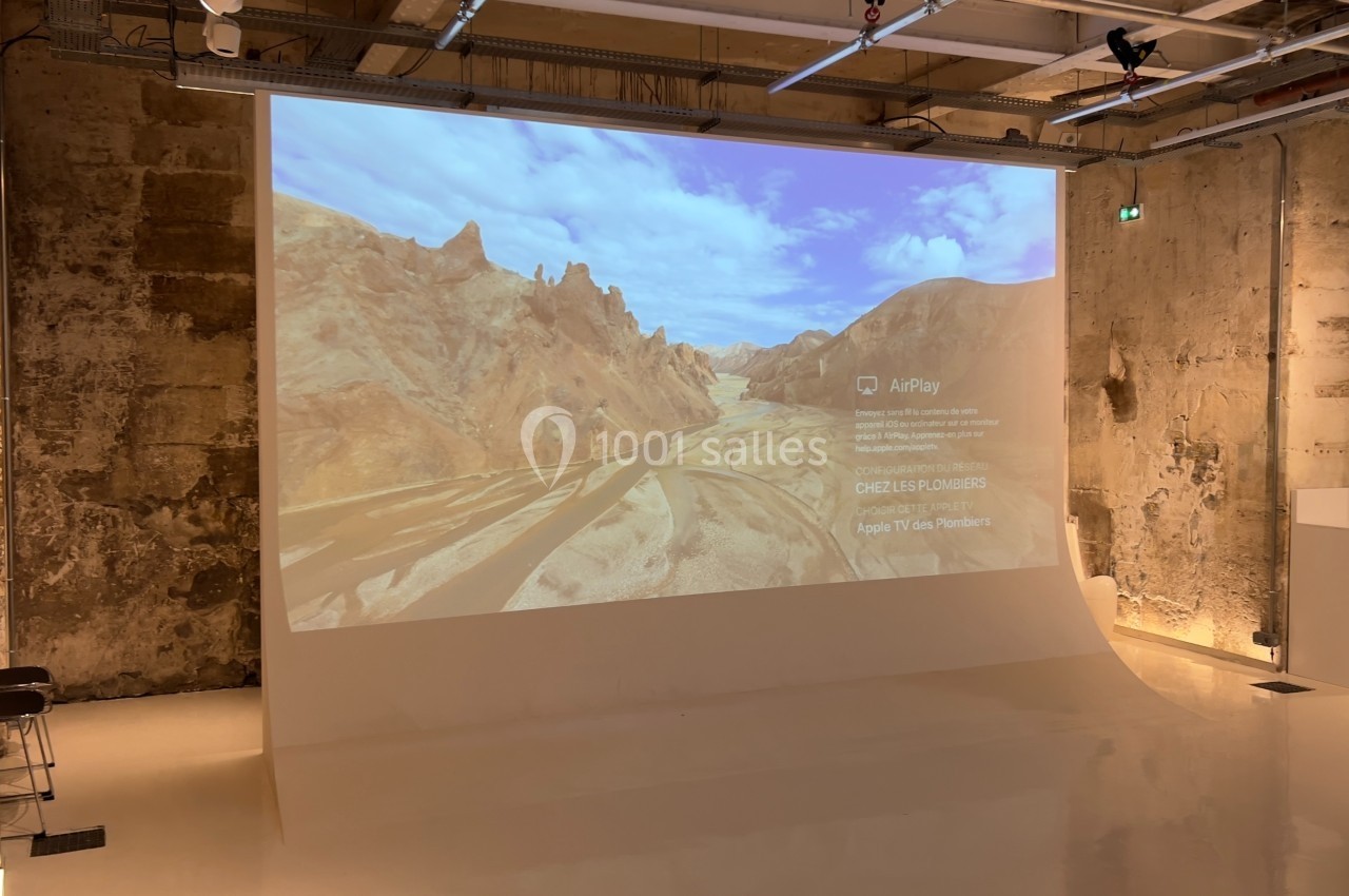 Projection d'un paysage désertique avec montagnes sous un ciel bleu, affichée sur un mur dans un espace industriel.