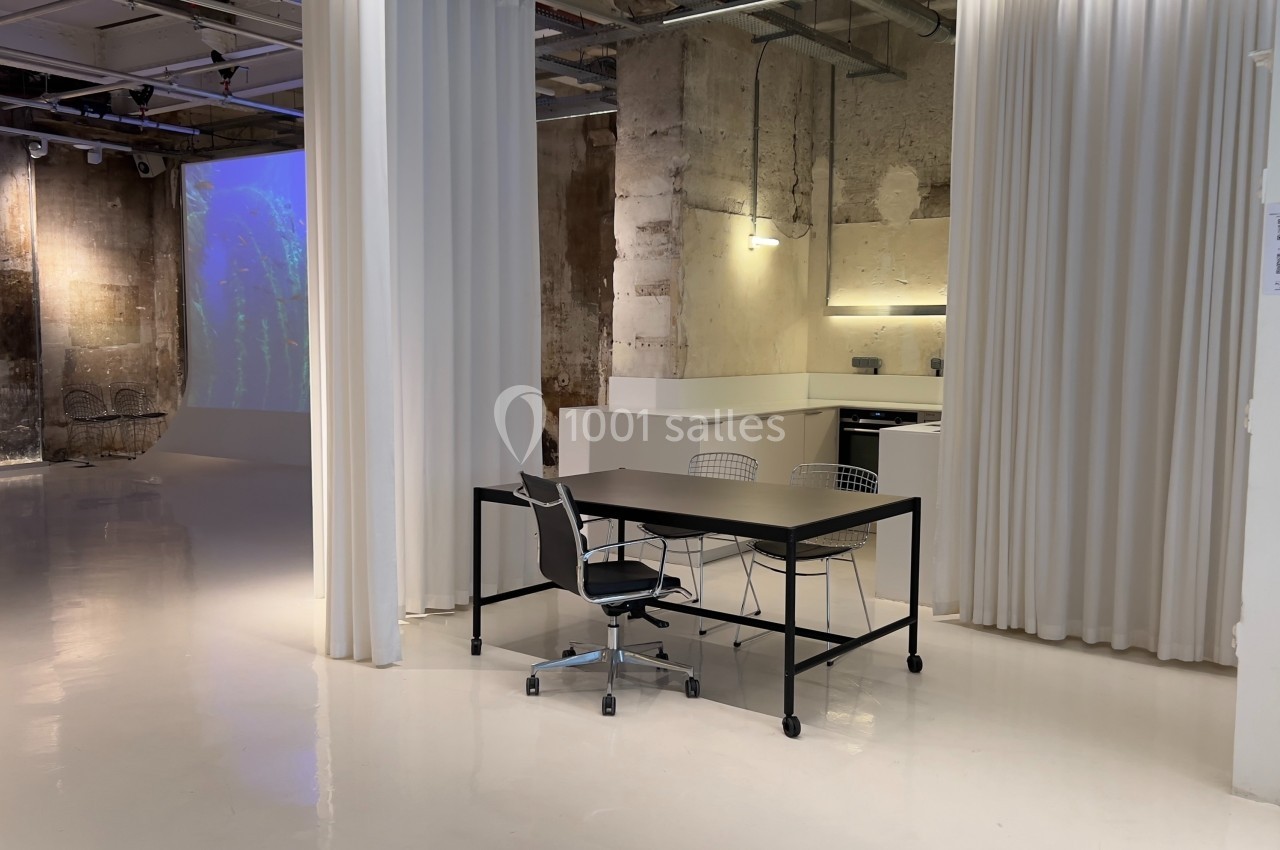 Espace intérieur moderne avec murs bruts, sol brillant, rideaux blancs et mobilier minimaliste.