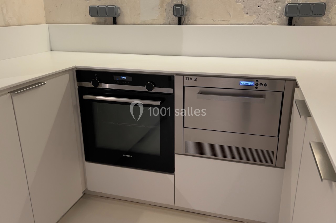 Cuisine moderne avec four encastré noir et machine à glaçons en inox intégrée dans des meubles blancs.