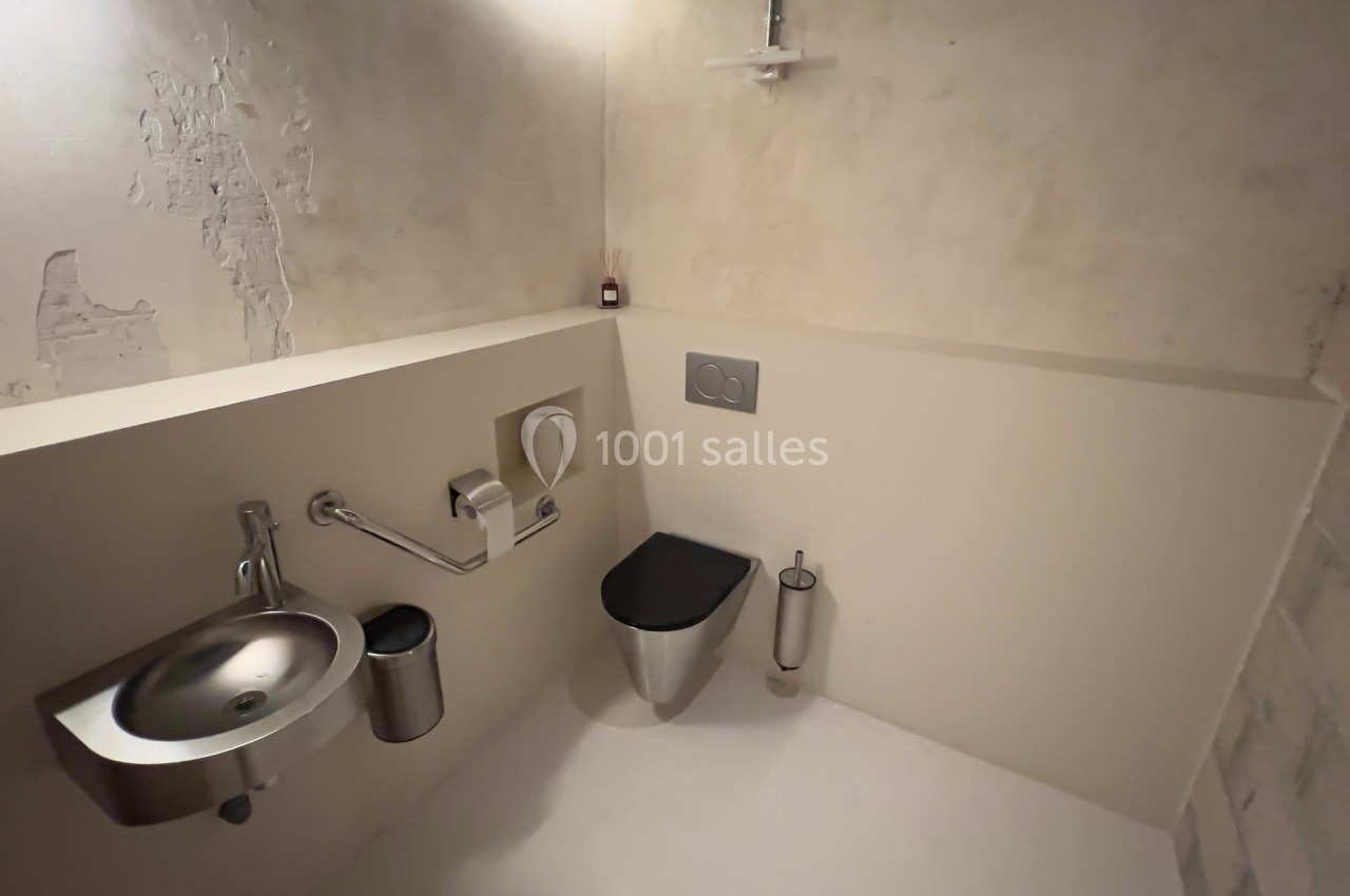Toilettes modernes avec murs en béton brut, lavabo en acier inoxydable et accessoires minimalistes.