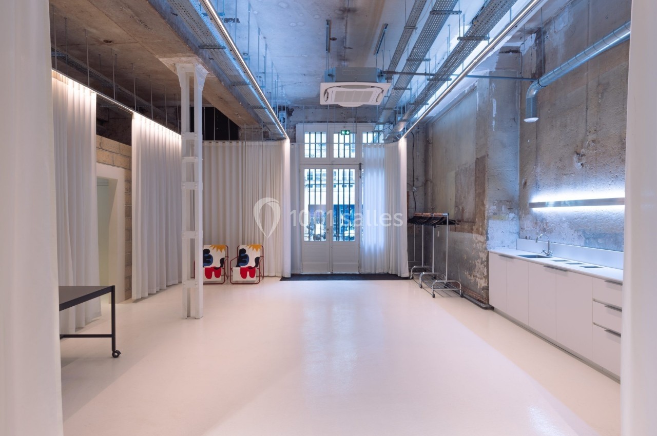Intérieur d'un espace moderne avec murs bruts, sol clair, mobilier minimaliste et grandes fenêtres vitrées.