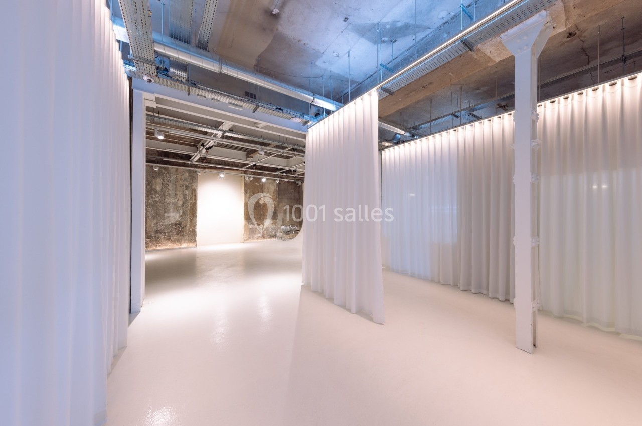 Vue intérieure d'un espace moderne avec sol clair, rideaux blancs suspendus et plafond industriel apparent.