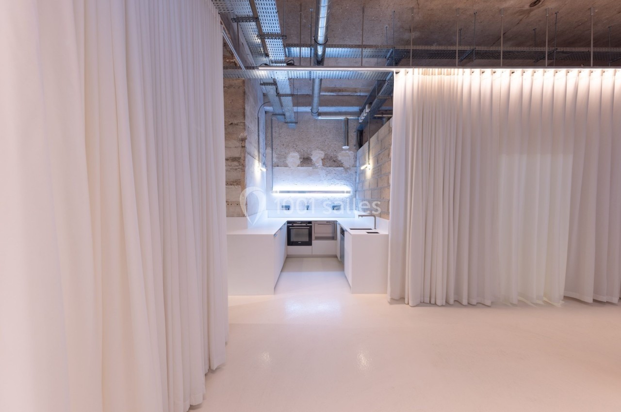 Cuisine moderne minimaliste avec plan de travail blanc, éclairage intégré et rideaux blancs entourant l'espace.