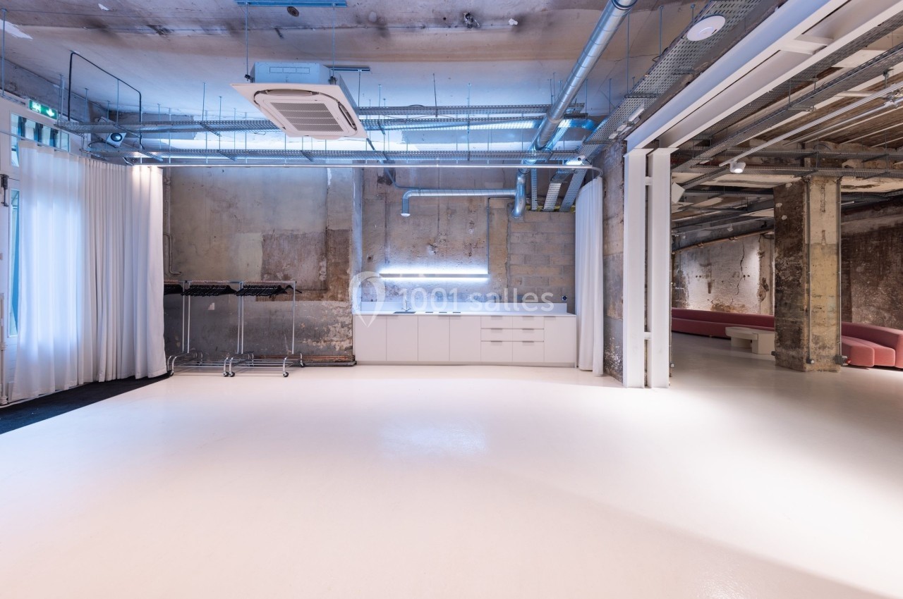 Espace intérieur industriel avec murs bruts, sol clair, éclairage moderne et mobilier minimaliste.