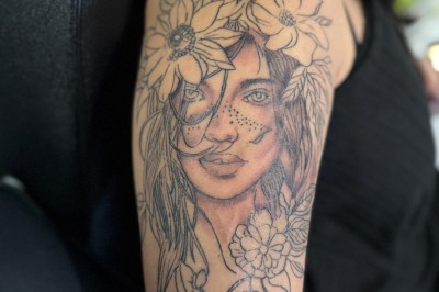 Tatouage floral noir et gris sur une cuisse, représentant des fleurs et des feuilles avec des détails délicats.