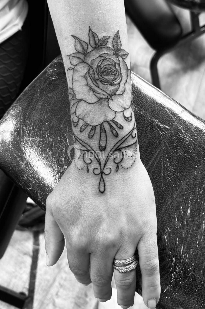 Tatouage en noir et blanc d'une rose avec des motifs décoratifs sur l'avant-bras d'une personne.