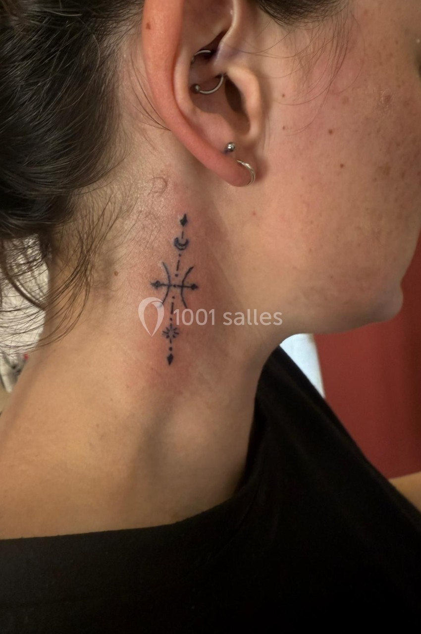Tatouage noir minimaliste sur le côté du cou d'une femme, représentant des motifs géométriques et symboliques.