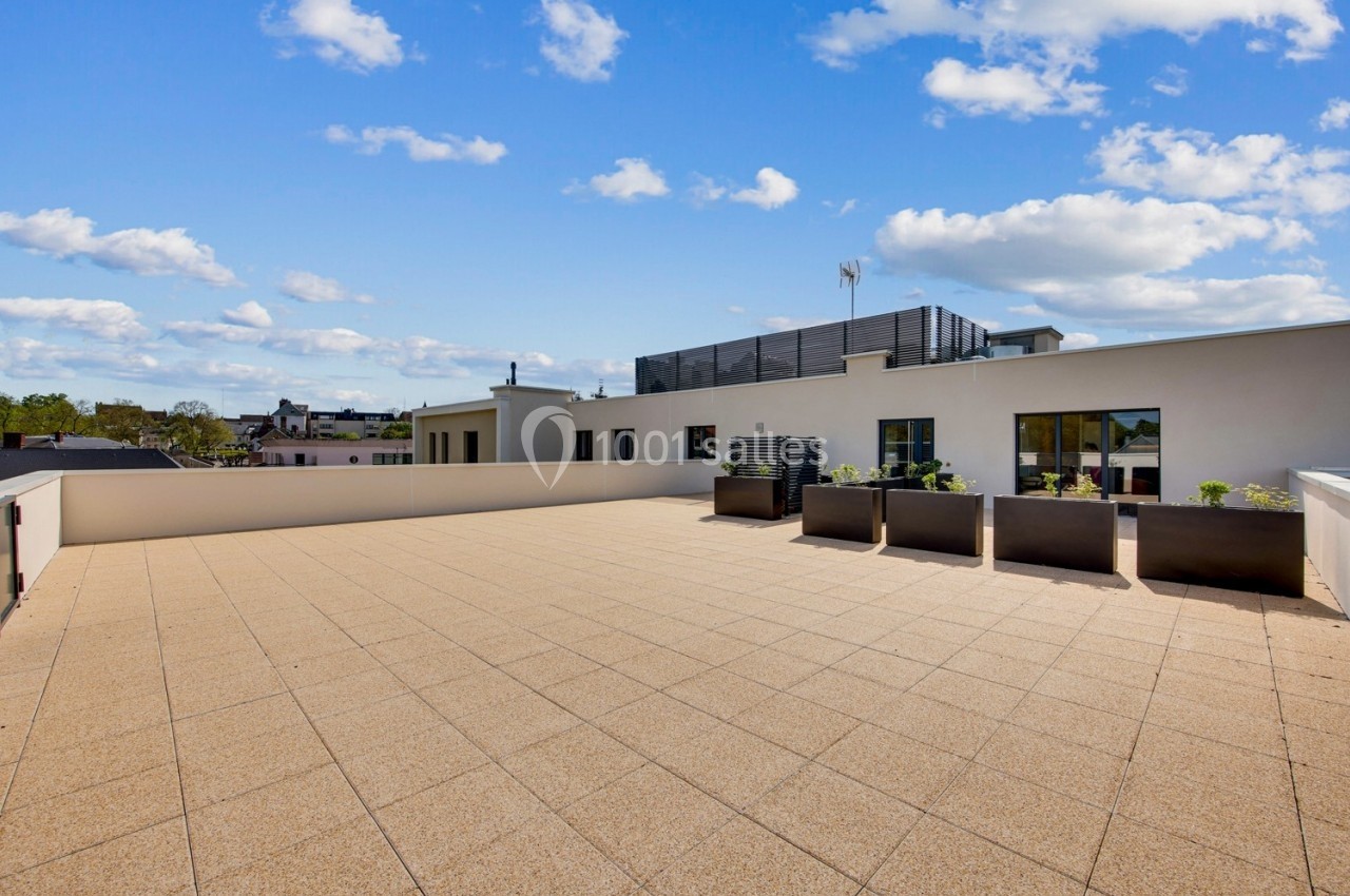 Grande terrasse en carrelage beige avec jardinières et vue dégagée sur des bâtiments modernes sous un ciel bleu.