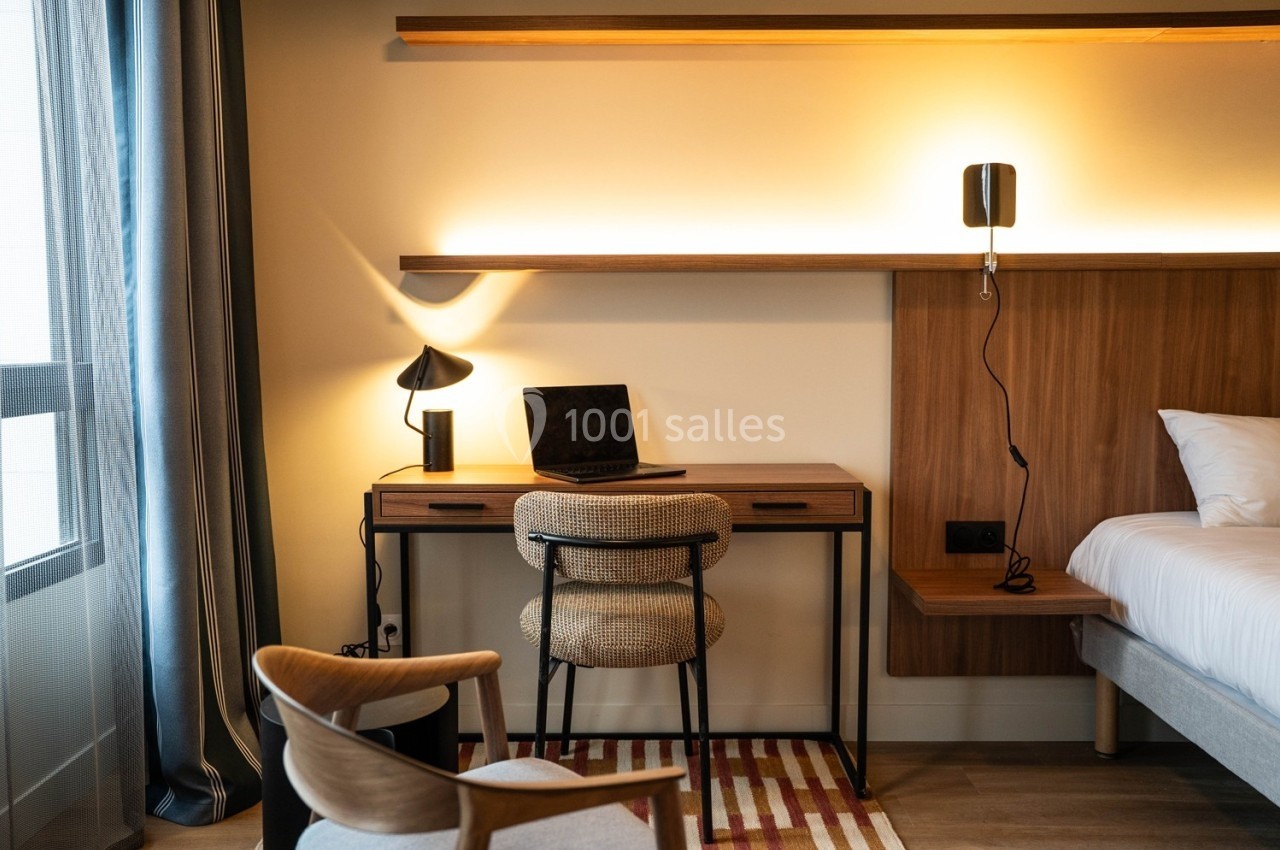 Bureau en bois avec ordinateur portable, lampe et chaise, situé dans une chambre moderne éclairée par une lumière douce.