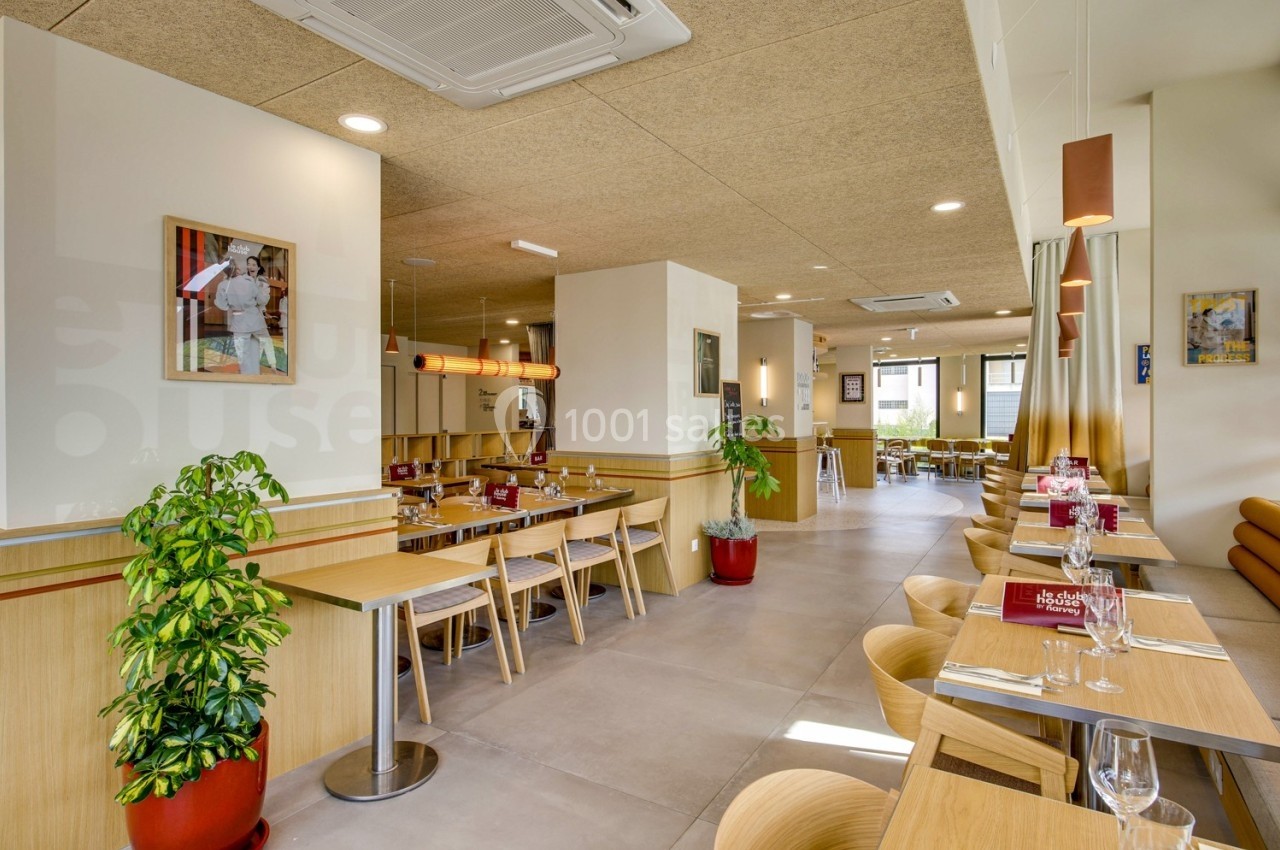 Salle de restaurant lumineuse avec tables en bois, chaises assorties, plantes décoratives et grandes baies vitrées.
