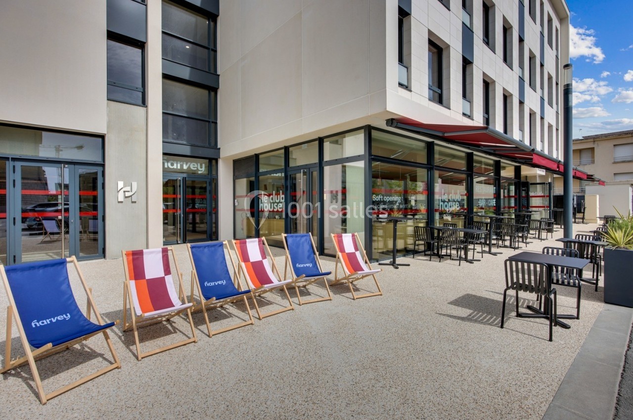 Façade moderne avec terrasse aménagée, chaises longues colorées et tables en extérieur devant un bâtiment vitré.