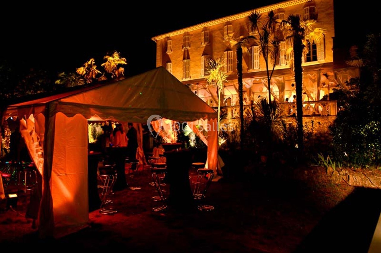 Tente éclairée et mobilier de réception en extérieur devant un bâtiment illuminé de nuit.