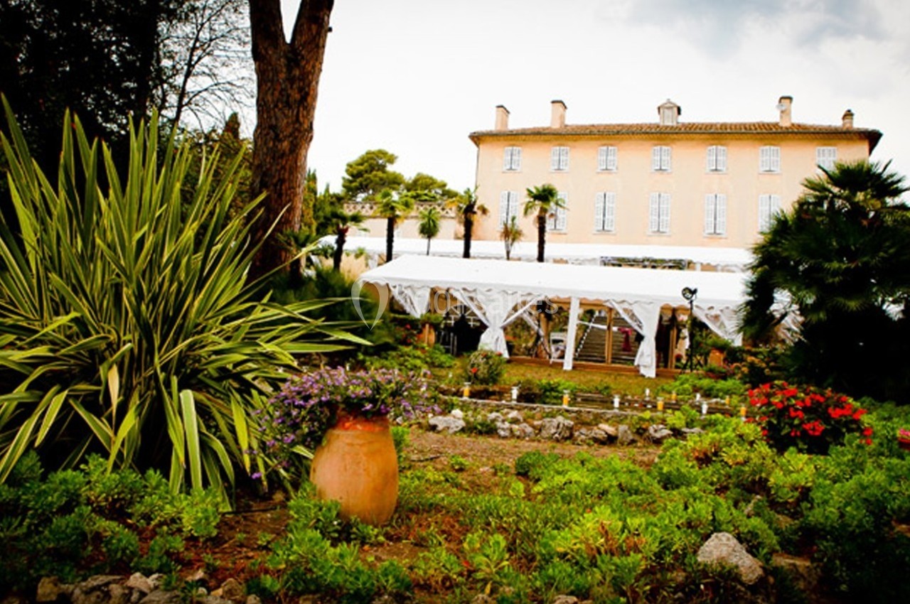 Jardin fleuri avec des plantes méditerranéennes devant un grand bâtiment en pierre de style classique.