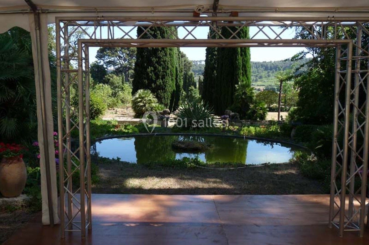 Vue d'un jardin avec un petit bassin rond entouré de végétation, encadré par une structure métallique.
