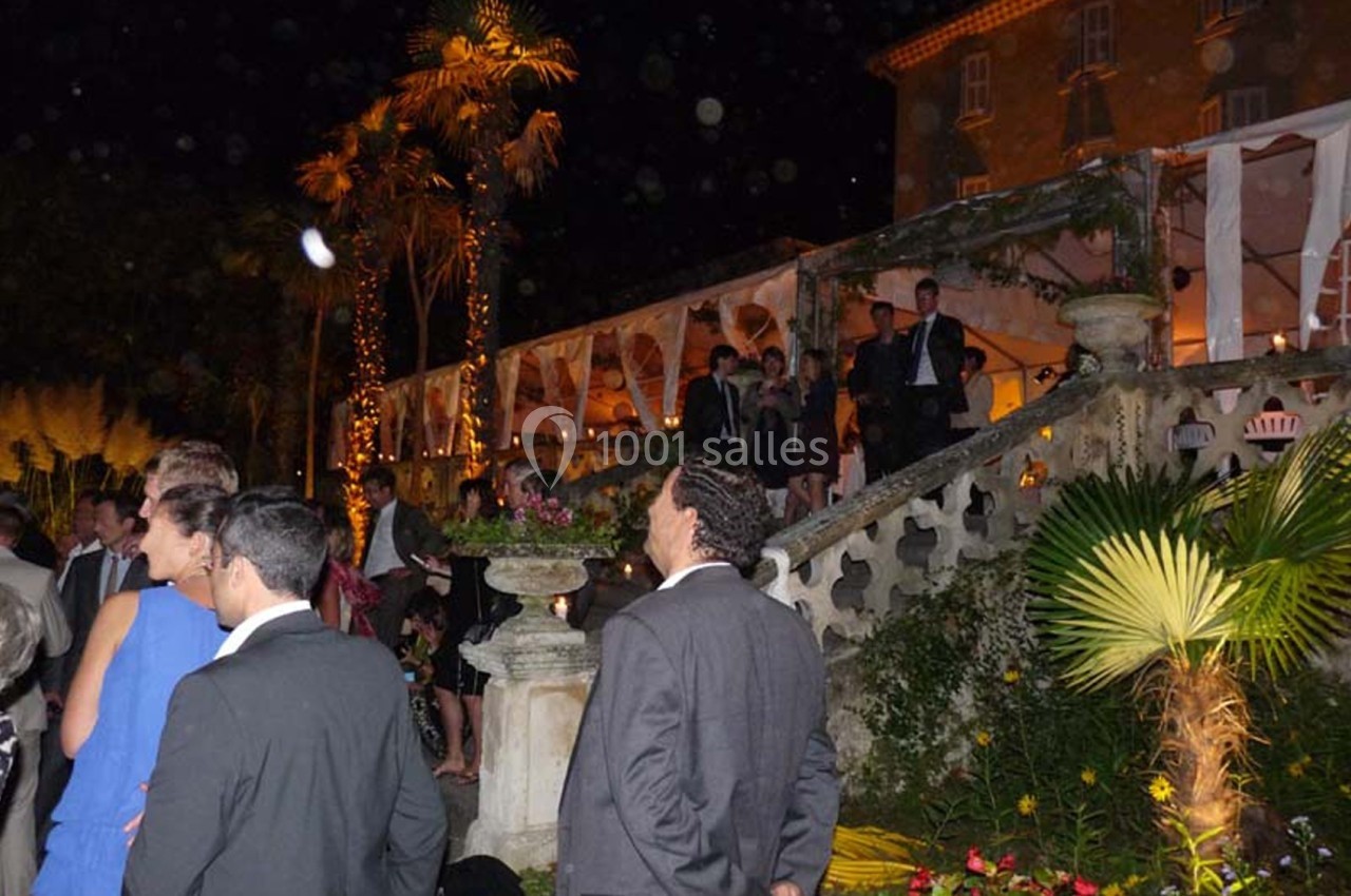 Groupe de personnes en tenue de soirée discutant près d'un escalier extérieur éclairé, entouré de végétation.