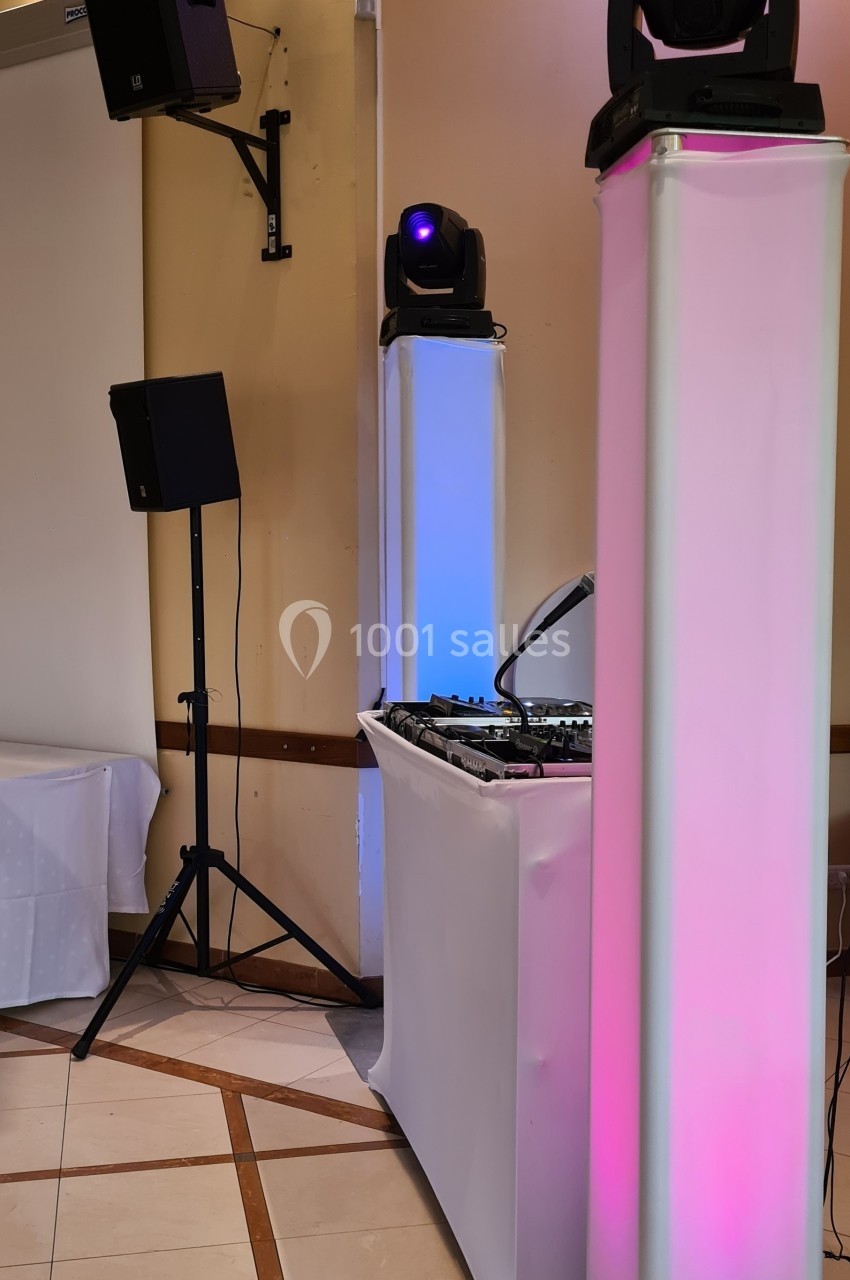Équipement de sonorisation et d'éclairage installé dans une salle, avec des colonnes lumineuses et une table de mixage.