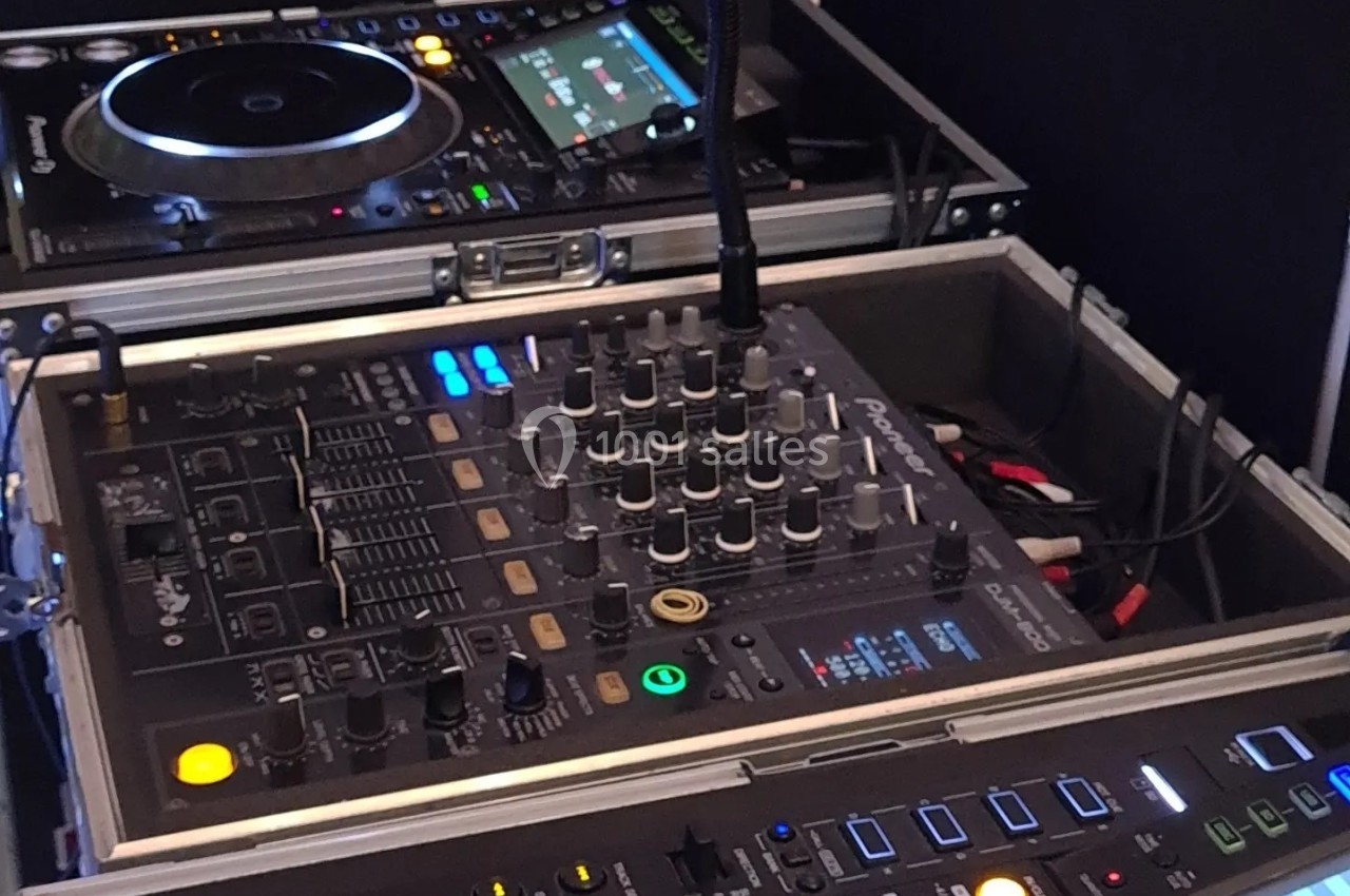 Table de mixage et platines DJ avec boutons et écrans lumineux, installées dans un espace de travail.