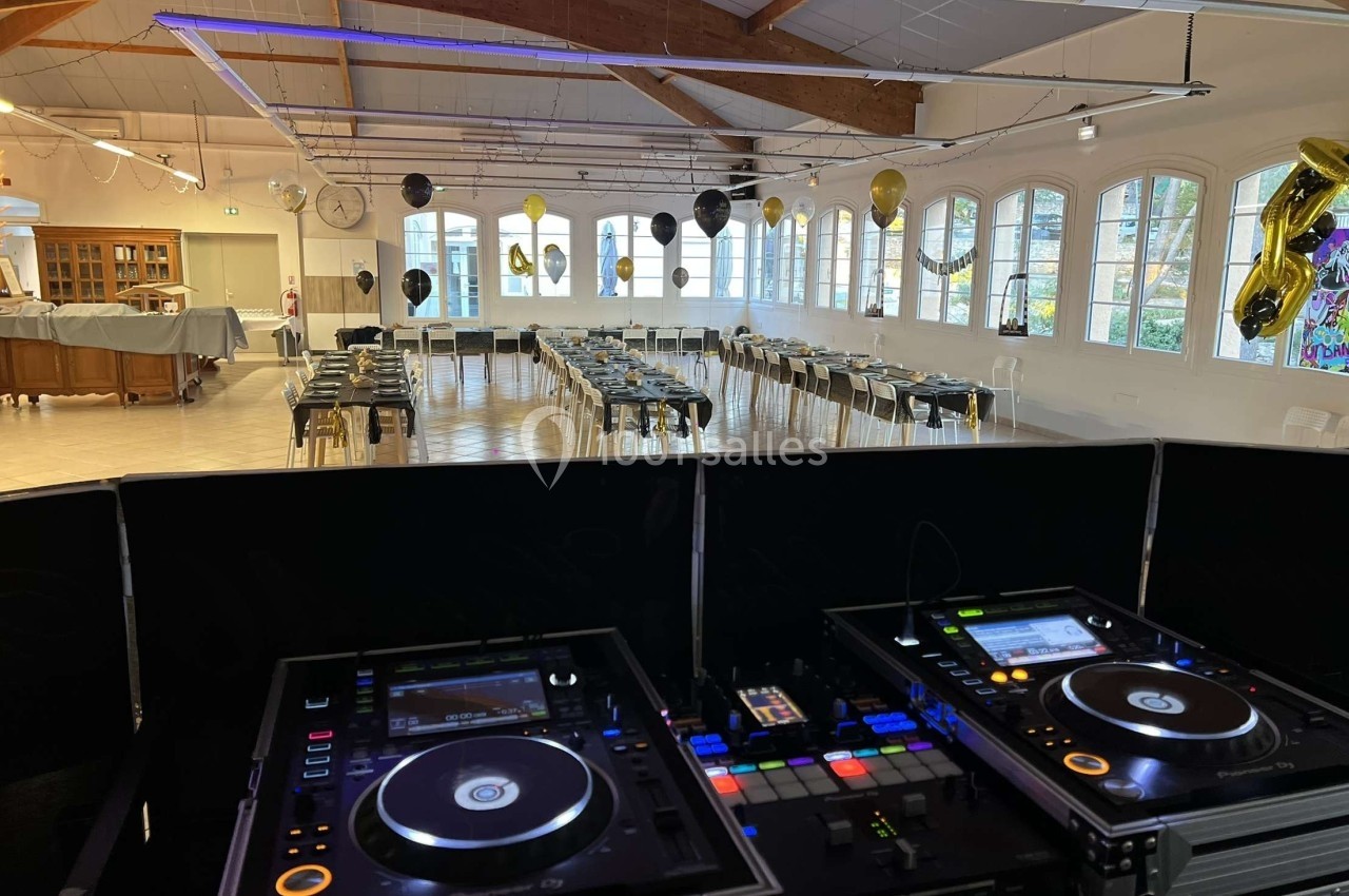 Salle décorée pour un événement avec tables dressées et ballons, vue depuis une table de mixage en premier plan.