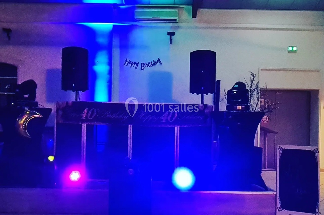 Salle décorée pour une fête avec éclairages colorés, enceintes et une bannière indiquant ’Happy Birthday’.