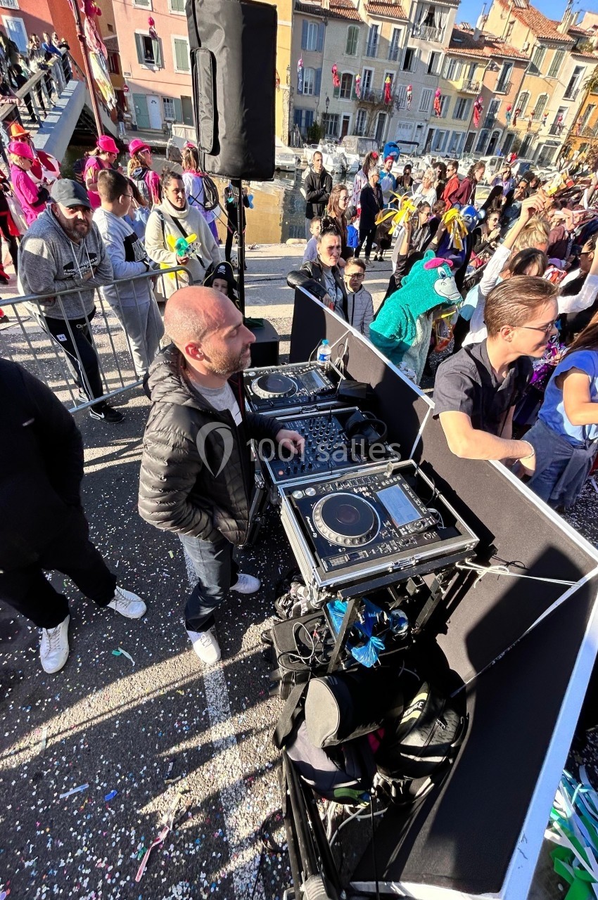 Un DJ anime une fête en plein air, entouré de participants déguisés dans une ambiance festive et colorée.