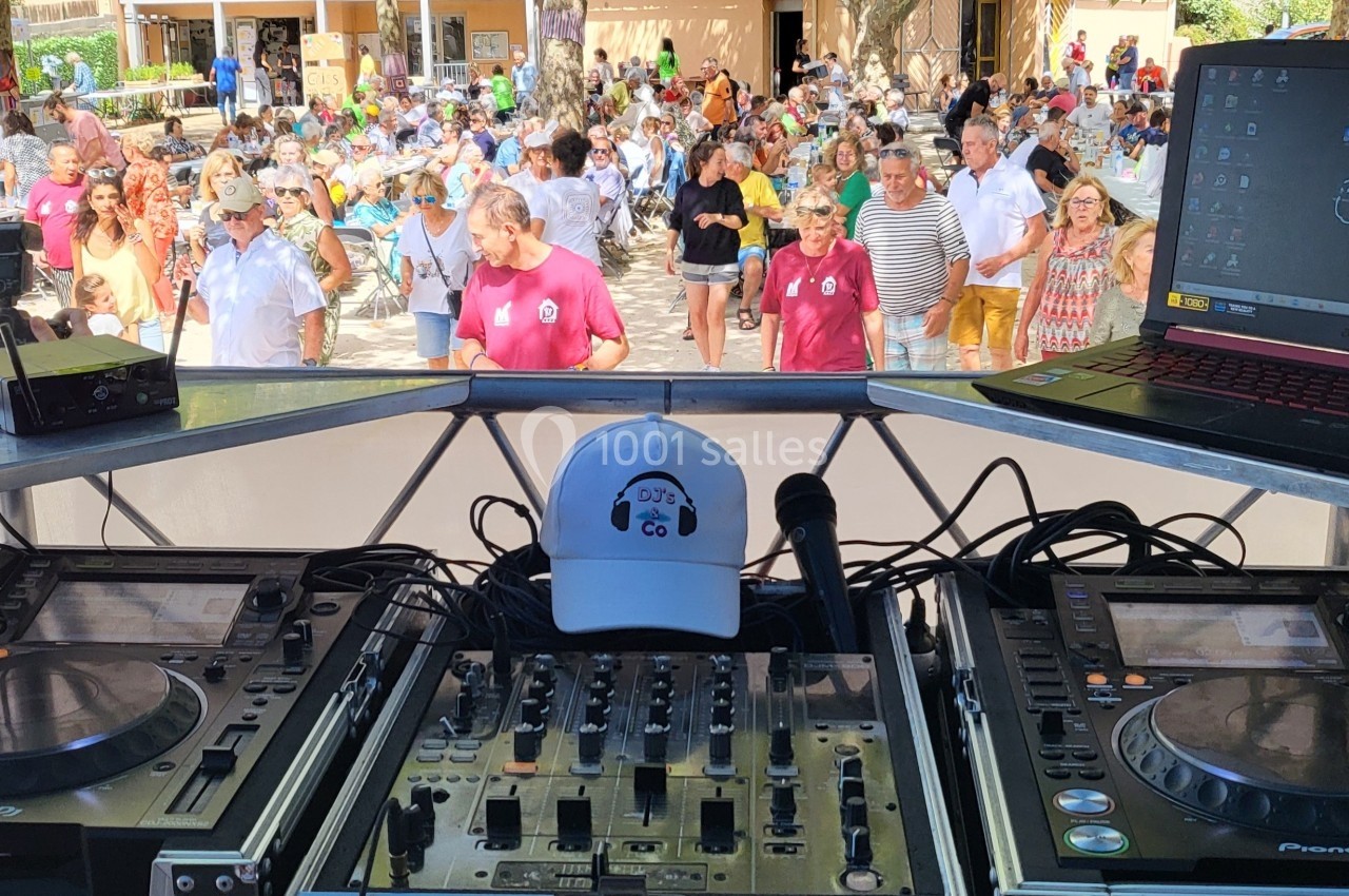 Vue depuis une table de mixage avec platines et ordinateur, face à une foule participant à un événement en plein air.