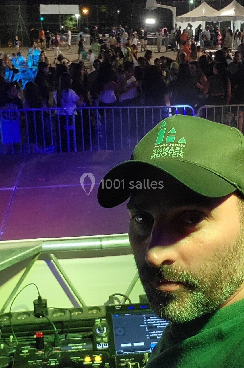 Un DJ mixe sur une scène en plein air, face à une foule rassemblée pour un événement nocturne.