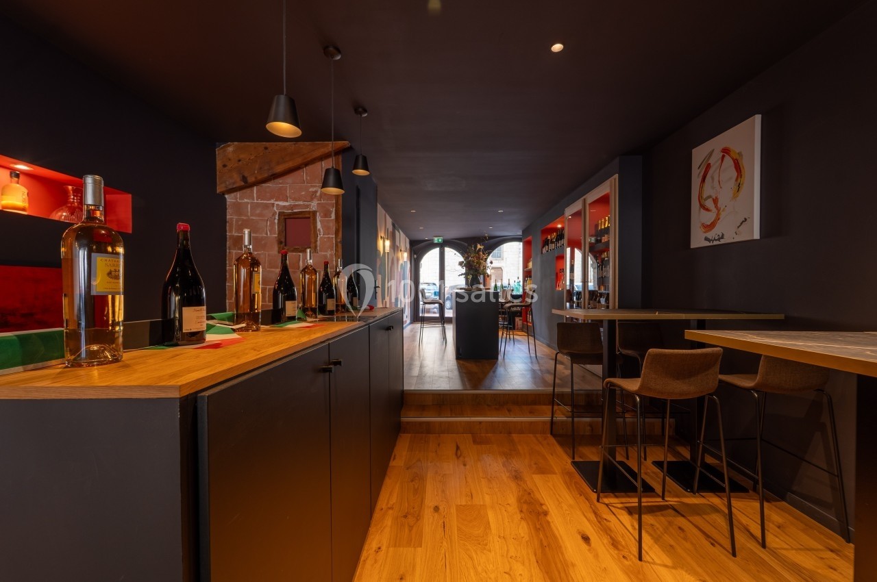 Intérieur d'un bar moderne avec comptoir en bois, bouteilles exposées et éclairage tamisé.